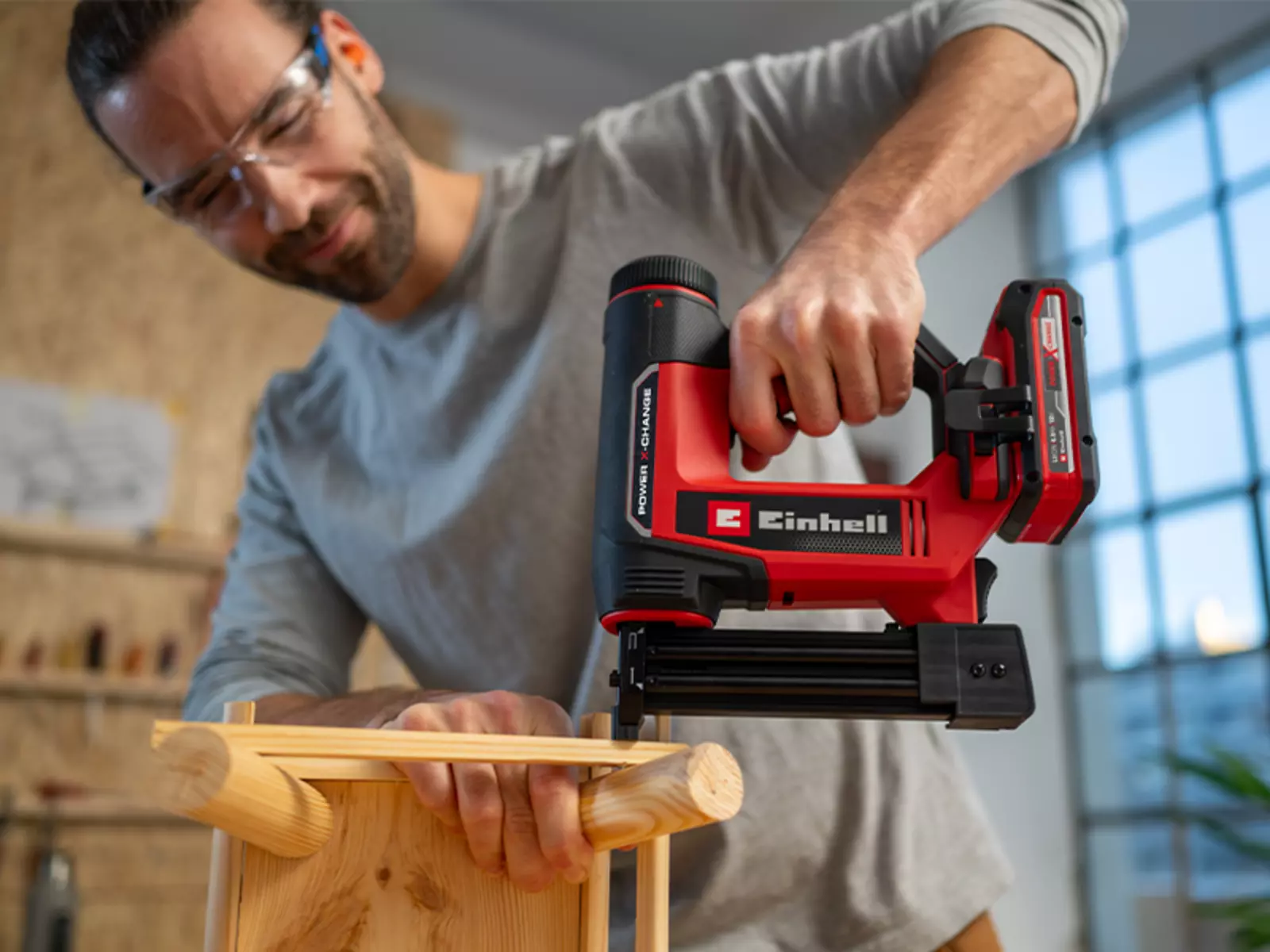 Чоловік скріплює дерев'яні компоненти акумуляторним цвяхозабивним пістолетом Einhell TE-CN 18/32 Li – Solo під час складання меблів у майстерні.