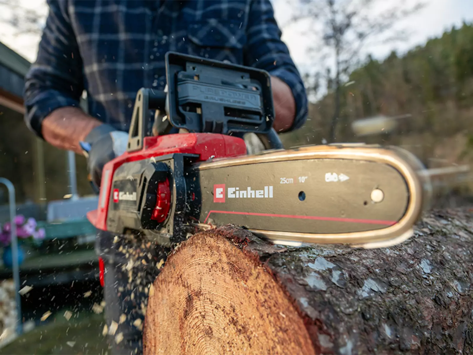 Крупный план: аккумуляторная цепная пила Einhell GE-LC 18/25 Li BL распиливает ствол дерева, летят щепки.