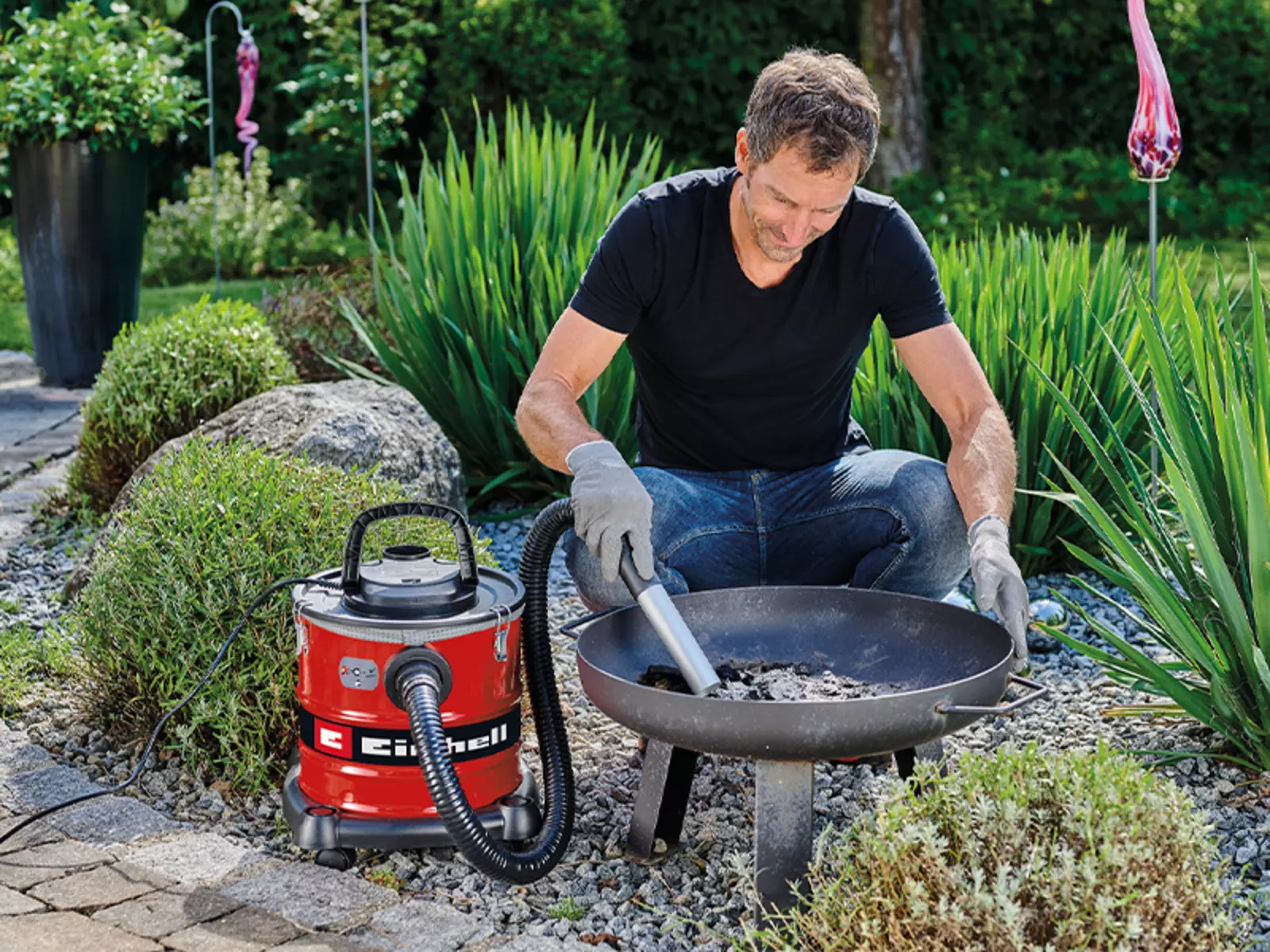 Чоловік використовує пилосос для золи Einhell TC-AV 2032 DW, щоб висмоктувати холодний попіл з вогнища в саду.