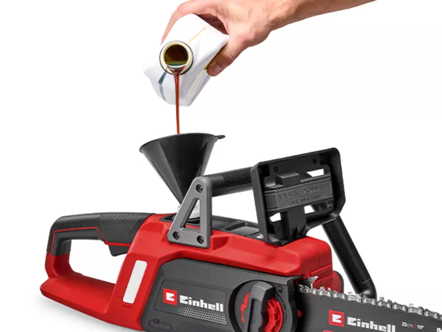 Рука заливает масло в масляный резервуар аккумуляторной бензопилы Einhell GE-LC 18/25 Li BL.